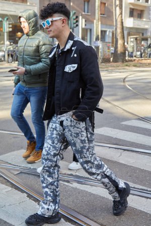Téléchargez les photos : MILAN, ITALIE - 13 JANVIER 2024 : Homme avec des lunettes de soleil blanches, une veste en denim noir et un pantalon avec des taches avant le défilé Dolce et Gabbana, Milan Fashion Week street style - en image libre de droit
