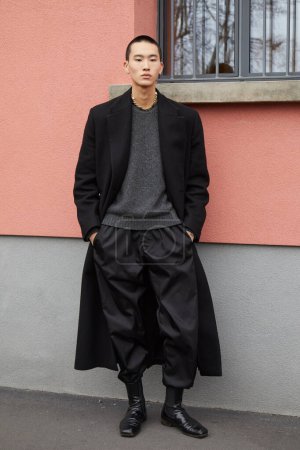Téléchargez les photos : MILAN, ITALIE - 14 JANVIER 2024 : Homme avec manteau noir, pantalon et pull gris avant le défilé K-Way, Milan Fashion Week street style - en image libre de droit