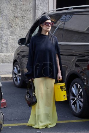 Foto de MILÁN, ITALIA - 21 DE FEBRERO DE 2024: Mujer con suéter negro y falda amarilla antes del desfile de moda Onitsuka Tiger, Milan Fashion Week street style - Imagen libre de derechos