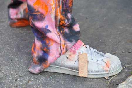 Foto de MILÁN, ITALIA - 21 DE FEBRERO DE 2024: Hombre con zapatillas Adidas Swlag y pantalones con colores de pintura antes del desfile de moda Fendi, Milan Fashion Week street style - Imagen libre de derechos