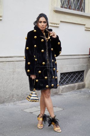 Foto de MILÁN, ITALIA - 21 DE FEBRERO DE 2024: Mujer con abrigo de piel negra con esferas doradas antes del desfile de moda Marco Rambaldi, Milan Fashion Week street style - Imagen libre de derechos