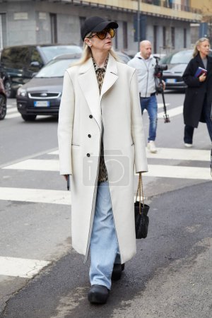 Téléchargez les photos : MILAN, ITALIE - 22 FEVRIER 2024 : Femme avec manteau blanc et pantalon en denim bleu avant le défilé Max Mara, Milan Fashion Week street style - en image libre de droit