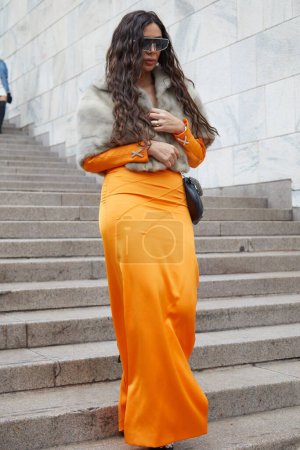 Foto de MILÁN, ITALIA - 22 DE FEBRERO DE 2024: Mujer con vestido naranja Genny y piel encogiéndose de hombros antes del desfile de moda Genny, Milan Fashion Week street style - Imagen libre de derechos