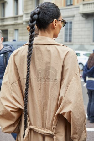 Téléchargez les photos : MILAN, ITALIE - 23 FÉVRIER 2024 : Femme avec tresse longue et trench coat beige avant Philosophie par Lorenzo Serafini défilé de mode, Milan Fashion Week street style - en image libre de droit