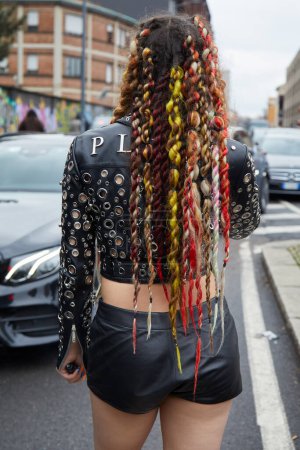 Foto de MILÁN, ITALIA - 23 DE FEBRERO DE 2024: Mujer trenzas coloridas y Philipp Plein chaqueta de cuero negro antes del desfile de moda de Gucci, Milan Fashion Week street style - Imagen libre de derechos