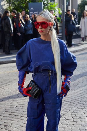 Téléchargez les photos : MILAN, ITALIE - 24 FÉVRIER 2024 : Denisa Palsha avec costume bleu et gants Ferrari rouges et lunettes de soleil avant le défilé de mode Ferrari, Milan Fashion Week street style - en image libre de droit