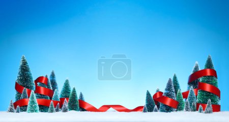 Téléchargez les photos : Pays des merveilles d'hiver avec des décorations miniatures d'arbres enveloppées dans un ruban rouge brillant sur la neige scintillante. - en image libre de droit
