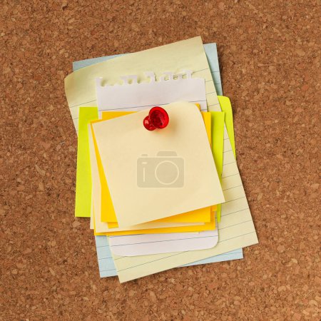 Téléchargez les photos : Pile de notes jaunes vides empilées et épinglées d'une pointe rouge. Espace de copie vide pour les avis, messages ou rappels importants du bureau. - en image libre de droit