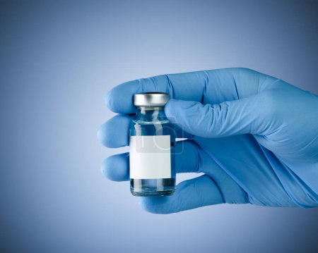 Foto de Mano en guantes médicos azules que sostienen un vial de vacuna con espacio en blanco para texto. Concepto sanitario con copyspace para texto. - Imagen libre de derechos