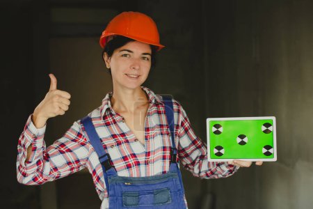 Téléchargez les photos : Femme constructeur en bleu salopettes pouces geste et vérifier le projet dans le nouveau bâtiment. concept de travail des femmes dans les professions masculines et égalité - en image libre de droit