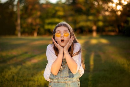 Photo for Surprised and excited school girl on lawn with green trees background - Royalty Free Image