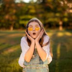 surprised and excited school girl on lawn with green trees background