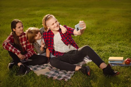 Téléchargez les photos : Deux frères avec soeur font selfie au téléphone sur l'herbe verte en été pique-nique ourdoors - en image libre de droit