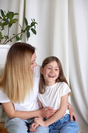 Photo for Mother and daughter in white T-shirts laughing at home - Royalty Free Image