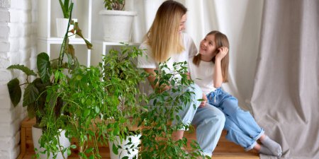 Photo for Focus on green houseplants mother and daughter talking on blurry background - Royalty Free Image