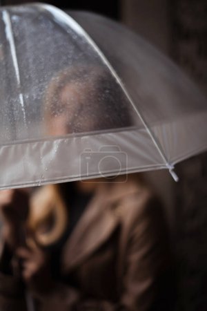 focus on rain drops on transparent umbrella in woman hands in rainy day. Urban solitude in rain