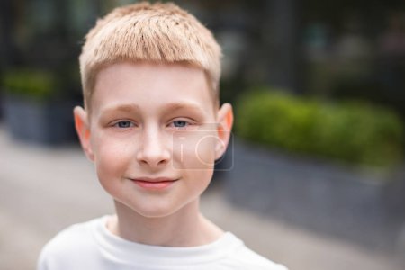Photo for Close up portrait of blond boy with blue eyes looking at camera and walking outdoors in city - Royalty Free Image