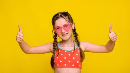 Téléchargez les photos : Fille portant des lunettes de soleil roses en forme de coeur fait pouce geste les deux mains - en image libre de droit