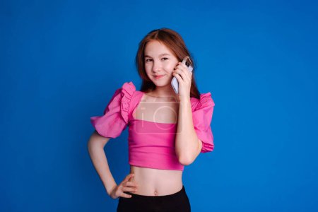 girl in pink top call on phone, looking at camera over blue background