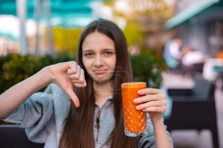 Téléchargez les photos : Malheureux adolescent fille montrer geste détester pouce vers le bas pour jus de citrouille - en image libre de droit