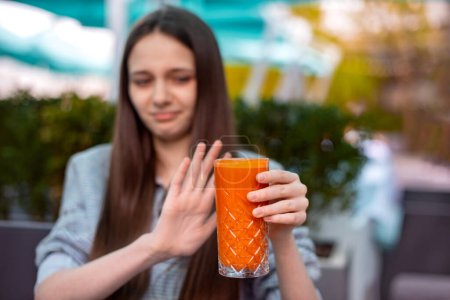 Téléchargez les photos : Se concentrer sur le verre avec du jus de carotte orange nutritionnel. adolescente déteste boire sainement. allergie aux ingrédients - en image libre de droit
