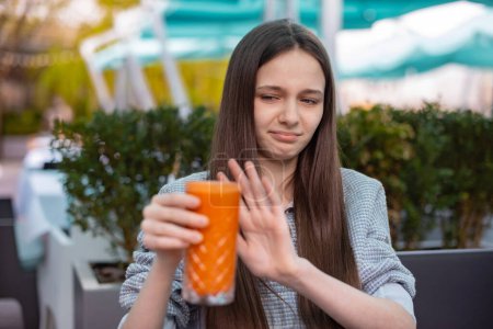 Téléchargez les photos : Fille refuse de boire de la carotte fraîche. adolescent fille montre un signe de refus de boisson nutritionnelle - en image libre de droit