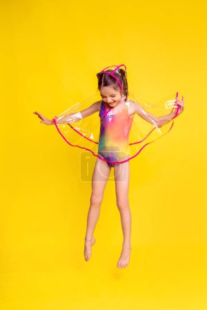 Téléchargez les photos : Drôle fille saut en imperméable transparent sur fond jaune. vêtements de confort pour Bali Wet Season Appeal - en image libre de droit