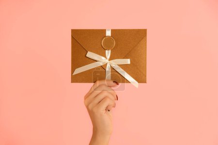 Téléchargez les photos : Femelle lever la main tenant certificat cadeau en bronze enveloppe cadeau sur fond rose - en image libre de droit