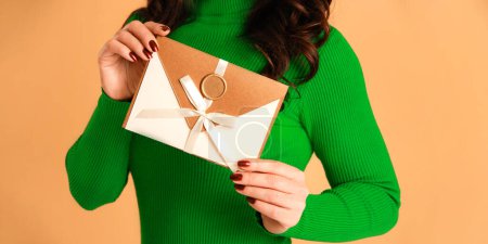 Téléchargez les photos : Chèque cadeau ou enveloppe de chèque en mains féminines sur fond beige - en image libre de droit