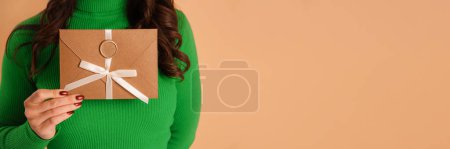 Téléchargez les photos : Chèque-cadeau en bronze élégante enveloppe dans les mains féminines sur fond beige - en image libre de droit