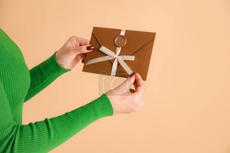Téléchargez les photos : Femme mains tenant Chèque-cadeau en bronze enveloppe élégante pour cadeau sur fond beige - en image libre de droit