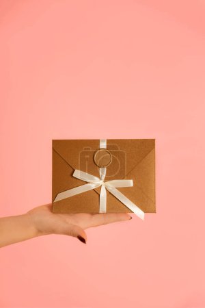 Téléchargez les photos : Femme main transmet Chèque-cadeau en bronze enveloppe cadeau sur fond rose - en image libre de droit