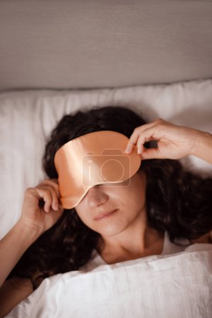 mujer quita la máscara de dormir de sus ojos en la mañana