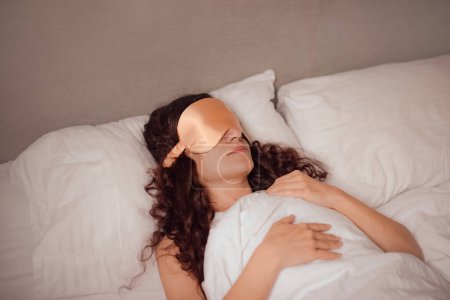 mujer en seda beige sueño máscara resto en la cama. sueño más profundo y reparador bloqueando cualquier luz no deseada