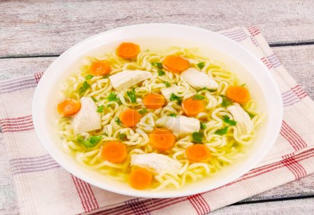 Homemade chicken soup with noodles and vegetables in a white bowl, on a  wooden background. Healthy warm comfortable food.