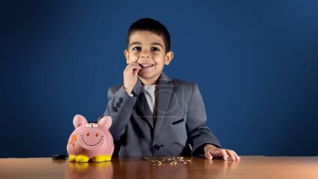 Photo for Cute child boy in suit biting on the coin. Child savings and growth of wealth concept. High quality photo - Royalty Free Image