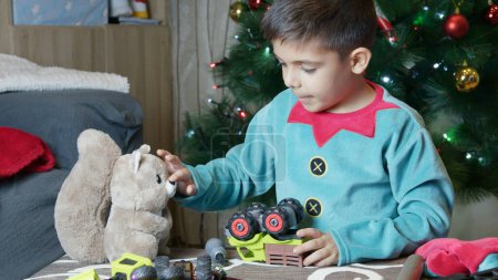 Foto de Lindo chico vestido de elfo acariciando su ardilla de juguete suave y montando juguetes en el taller de santas. Foto de alta calidad - Imagen libre de derechos
