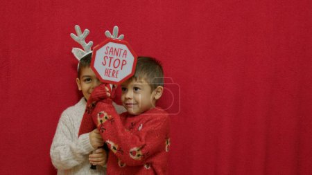 Cute kids brothers hugging and showing santa stop here sign. Christmas celebration and happy family. High quality photo