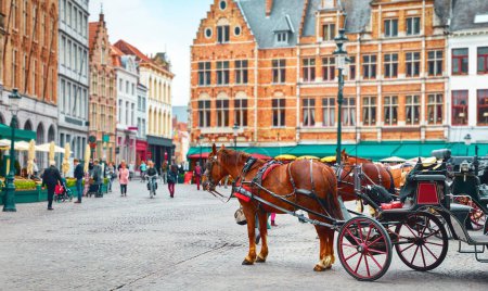 Foto de Bruges, Belgium. Market Square (Markt. Historical centre of old town. Carriages with horses waiting for touristic rides and city tours - Imagen libre de derechos
