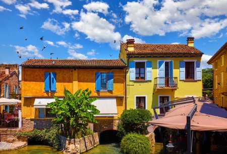 Téléchargez les photos : Old village Borghetto Valeggio sul Mincio, Veneto region, Italy. Colorful houses. Panoramic view at the town house on river. Sunny day with blue sky and clouds - en image libre de droit