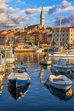 Photo for Rovinj, Istria, Croatia. Motorboats and boats on water in port of Rovigno. Medieval vintage houses old town. Yachts landing, high tower the Saint Euphemia Church. Morning sunrise blue sky with clouds - Royalty Free Image