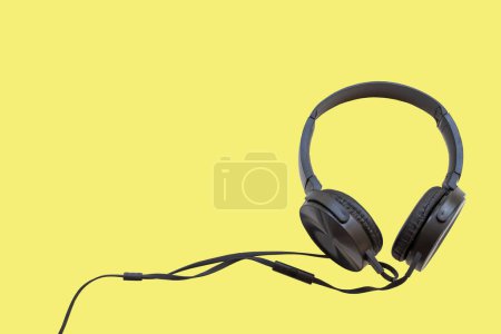 schwarzer Kopfhörer zum Hören von Lifestyle-Arrangement flach im Postkartenstil auf gelbem Hintergrund