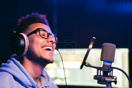 Photo for Male vocal artist, singer, podcaster with curly hair, headphones in sound studio recording new melody or album. - Royalty Free Image