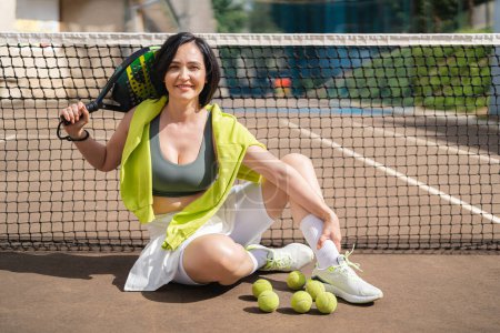 Photo for Adult woman padel player posing on the outdoor court splashed by the sunlight. Active sports concept. - Royalty Free Image