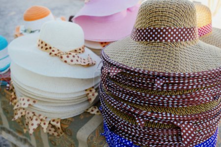 Téléchargez les photos : Une photo de différents chapeaux de différentes couleurs et styles empilés sur une table avec une nappe à motifs. La table est située sur une plage ou en plein air - en image libre de droit