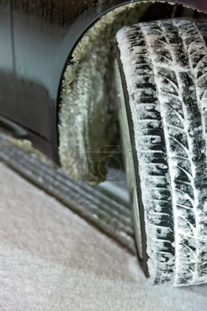 Téléchargez les photos : Angle vue de face des traces de pneus de voiture sur route enneigée la nuit. Saison d'hiver, glace sur le corps de la voiture. Concentration sélective - en image libre de droit