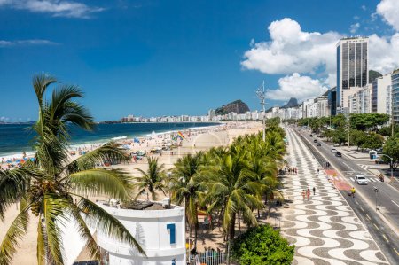 Téléchargez les photos : Copacabana Beach derrière les palmiers par le célèbre trottoir et la rue. Vue d'été avec ciel bleu, Rio de Janeiro, Brésil - en image libre de droit