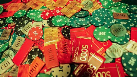 Téléchargez les photos : Gambling poker chips scattered haphazardly across a green poker table. The chaotic arrangement of the chips suggests a sense of addiction to the thrill of gaming. Shows a compulsive need to gamble. - en image libre de droit
