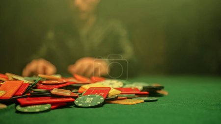 Téléchargez les photos : A chaotic scene of a poker game with chips scattered haphazardly across the table. Blurry background of a poker player sitting at the table. - en image libre de droit