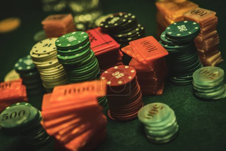 Téléchargez les photos : Poker chips are stacked neatly on a green textured table, the focus is on the chips with a shallow depth of field. The background is hazy with the smoke of cigars filling the room. - en image libre de droit